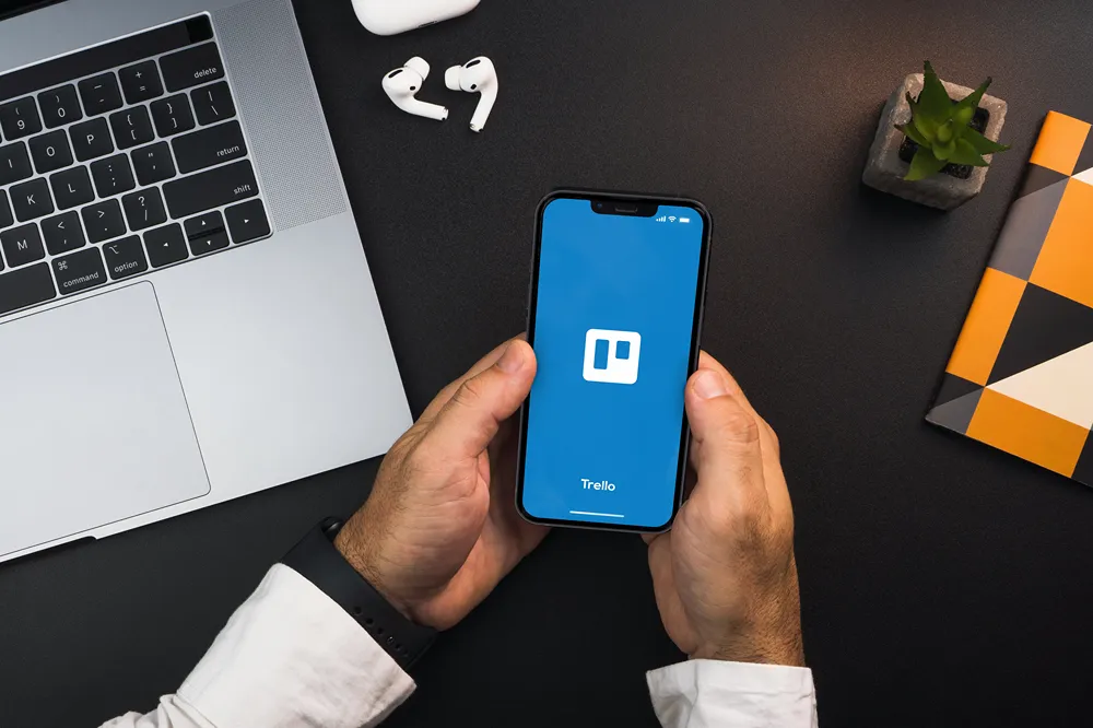 A person holding a smartphone with the Trello app open on it.