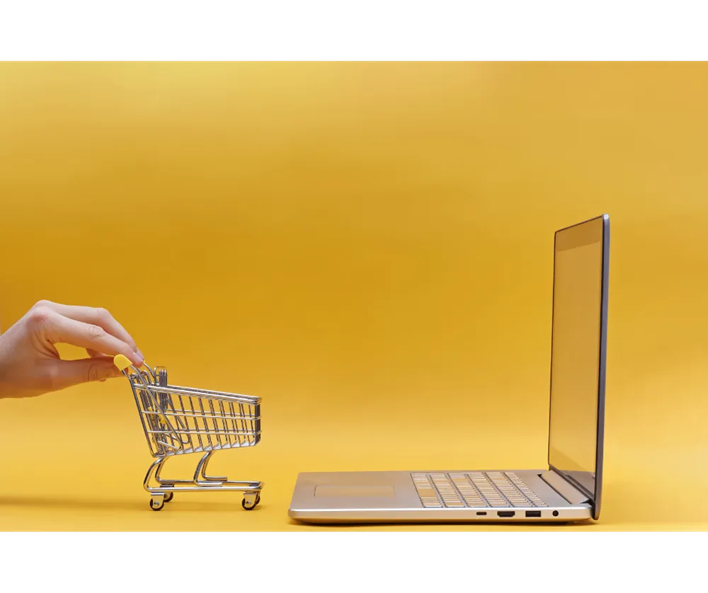 A small toy shopping cart in front of a laptop monitor