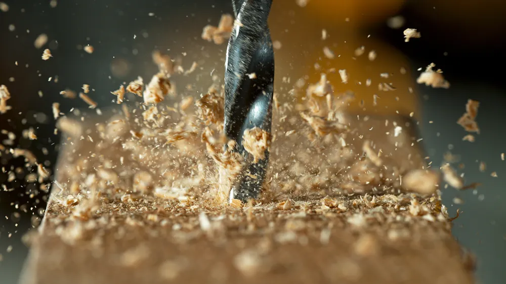 A wooden beam being drilled and throwing sawdust up into the air.