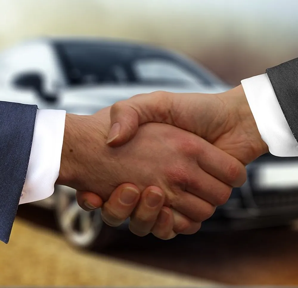 Two people shaking hands in front of a car.