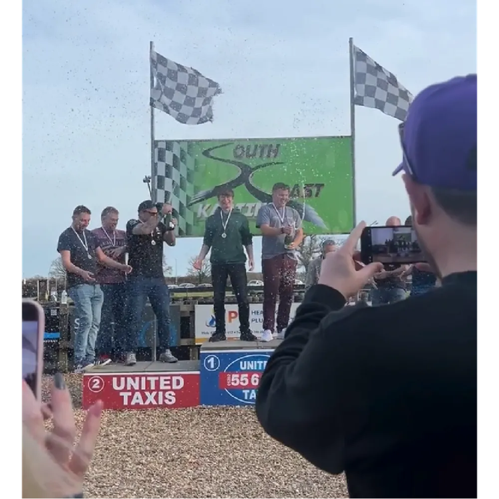 Cold Banana Agency Grand Prix 2025 Racers on the podium having won first place. People celebrate, popping champagne bottles.