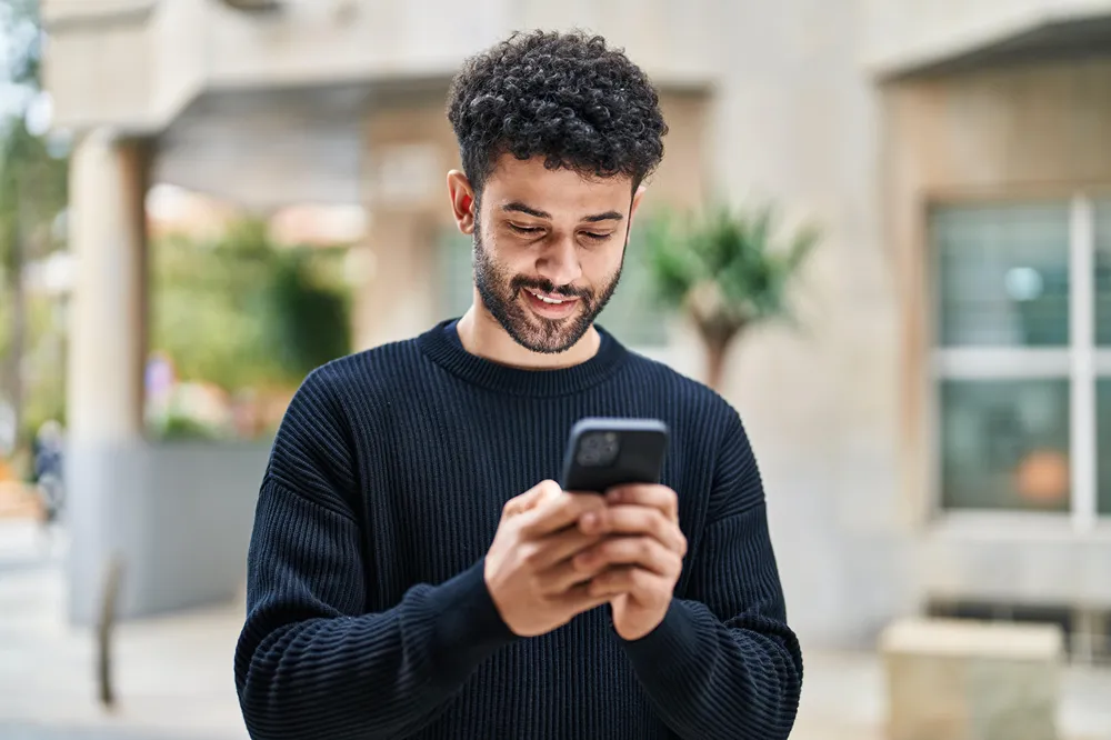 A person in a navy blue pullover looking at their smartphone.