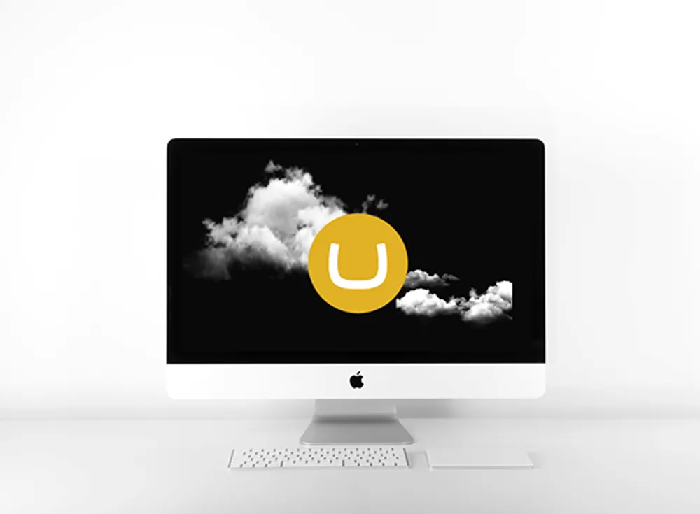 An Apple computer with a gold Umbraco glyph on the screen superimposed over white clouds