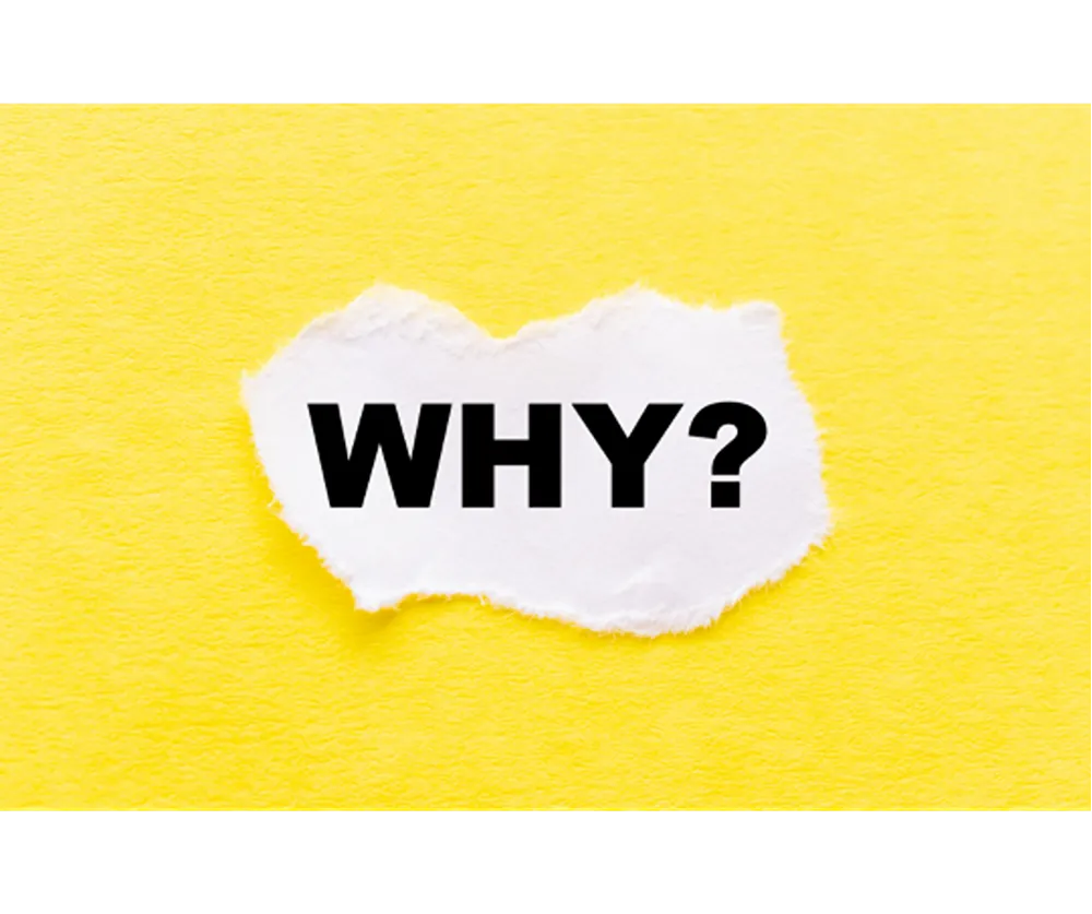 A scrap of paper with black text reading "Why?" on it on a background of textured yellow paper