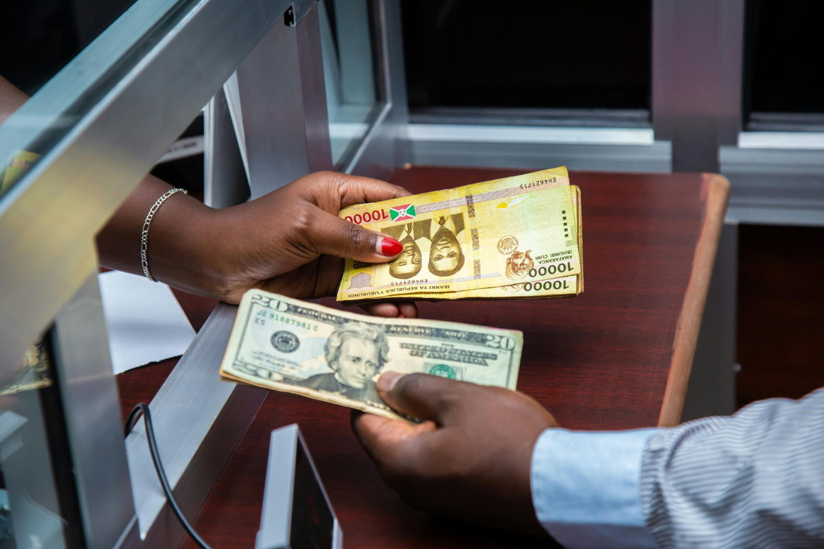 Two people handing each other different bank notes in a currency conversion booth.