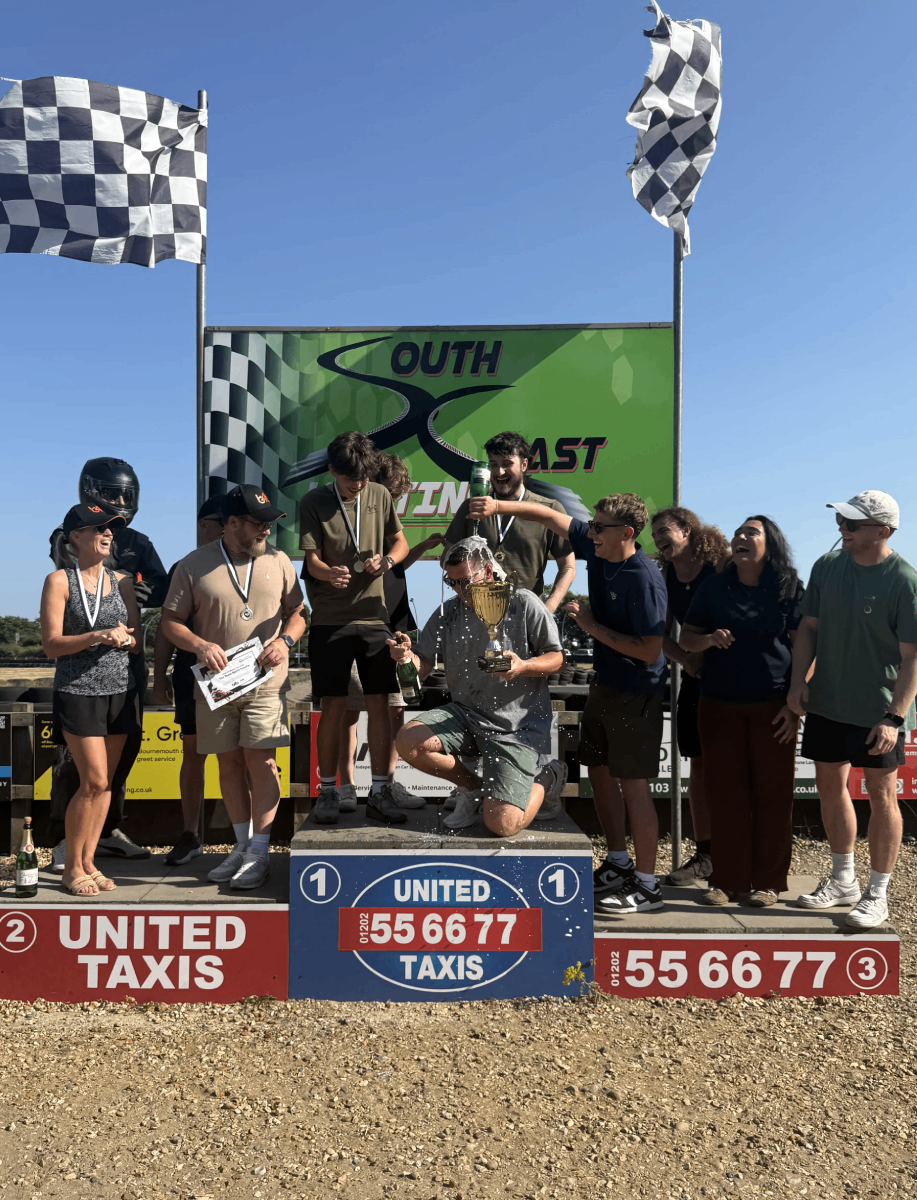 Cold Banana racers in first place on the podium, with third place podium winners pouring champagne over the CB racers in celebration.