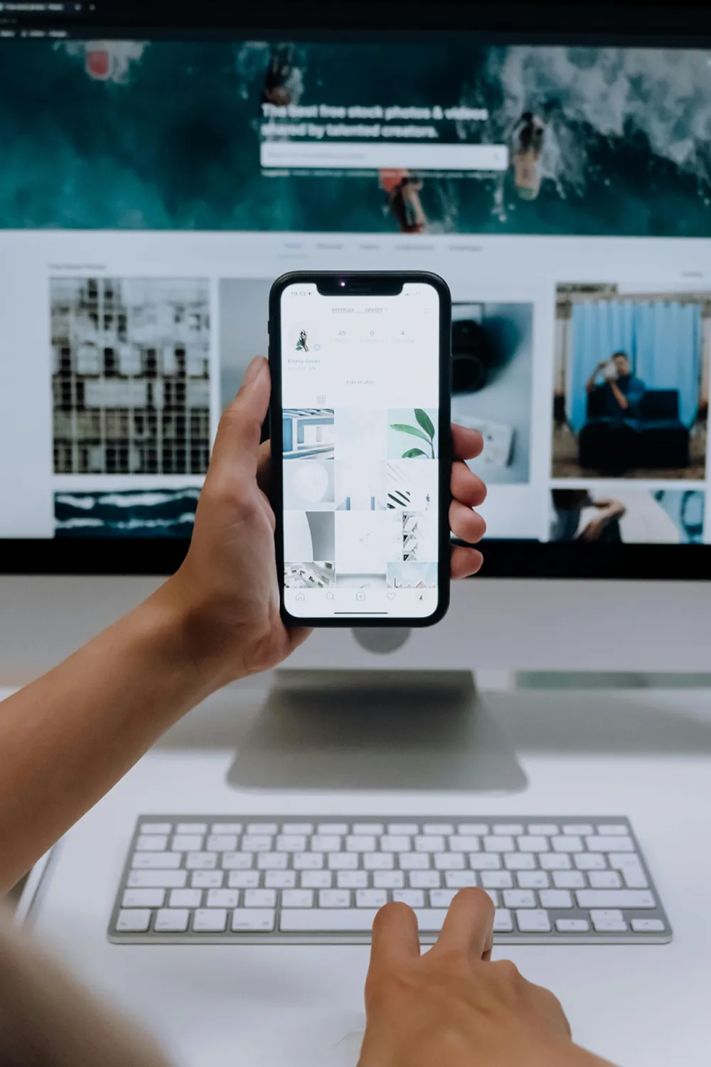 A person managing an Instagram feed on their smartphone, whilst also on their computer.