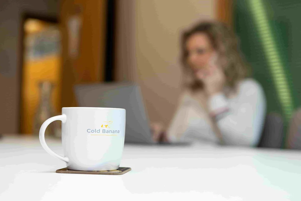 Cold Banana mug in a meeting room, with a Cold Banana employee taking a call in the background