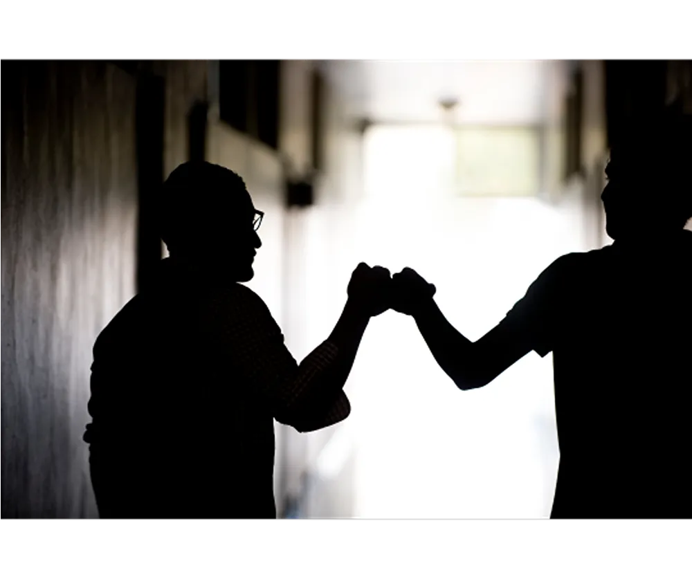 Silhouettes of two people fistbumping one another in an alley
