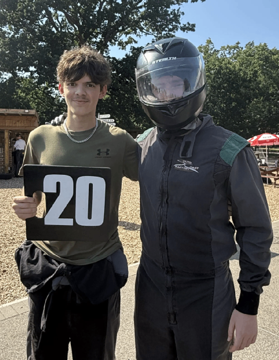 Two members of the Cold Banana AGP racing team, team member on the left holding the racing board to flag for pitstops, and the team member on the right fully suited for racing.