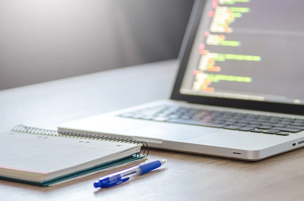 A notepad and a blue pen in front of an open laptop