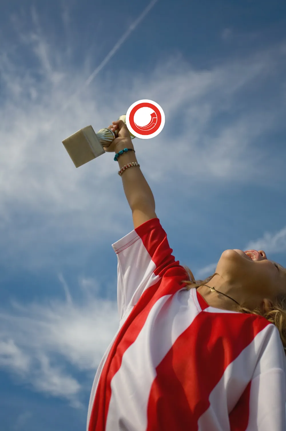 A footballer wearing a red and white striped football shirt holding a trophy aloft with the Sitecore logo on it.