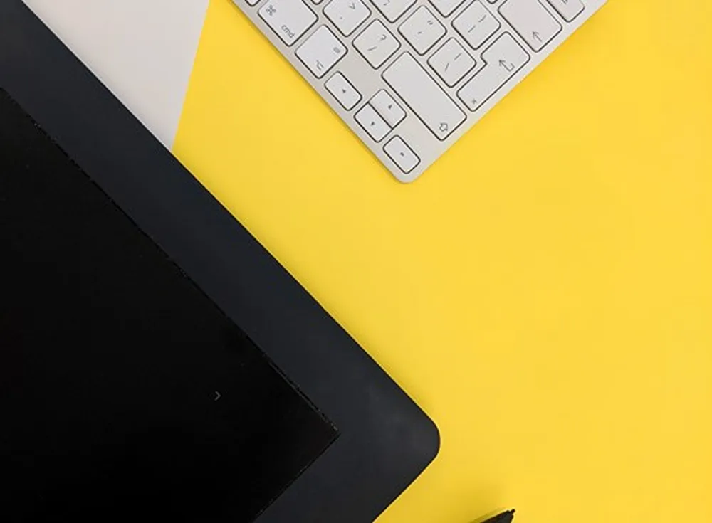 A laptop and a keyboard on a yellow tabletop