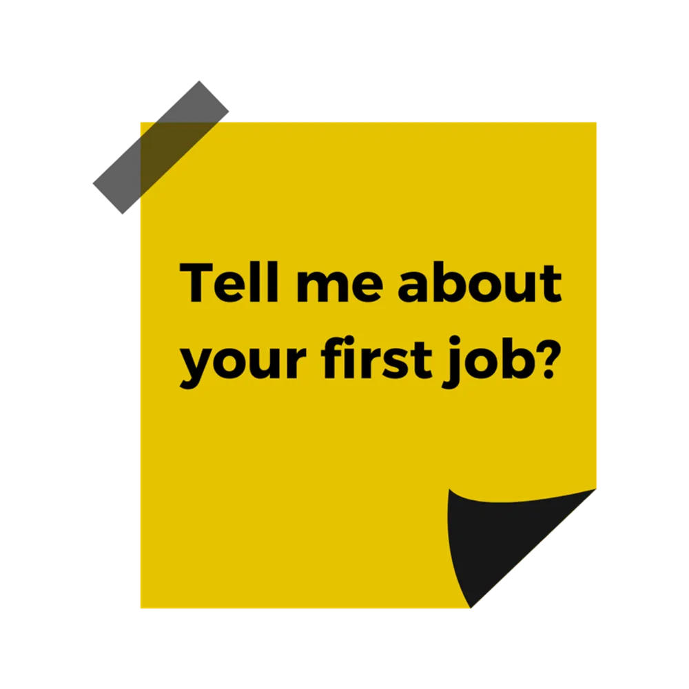 A yellow post it note with black text reading "Tell me about your first job"