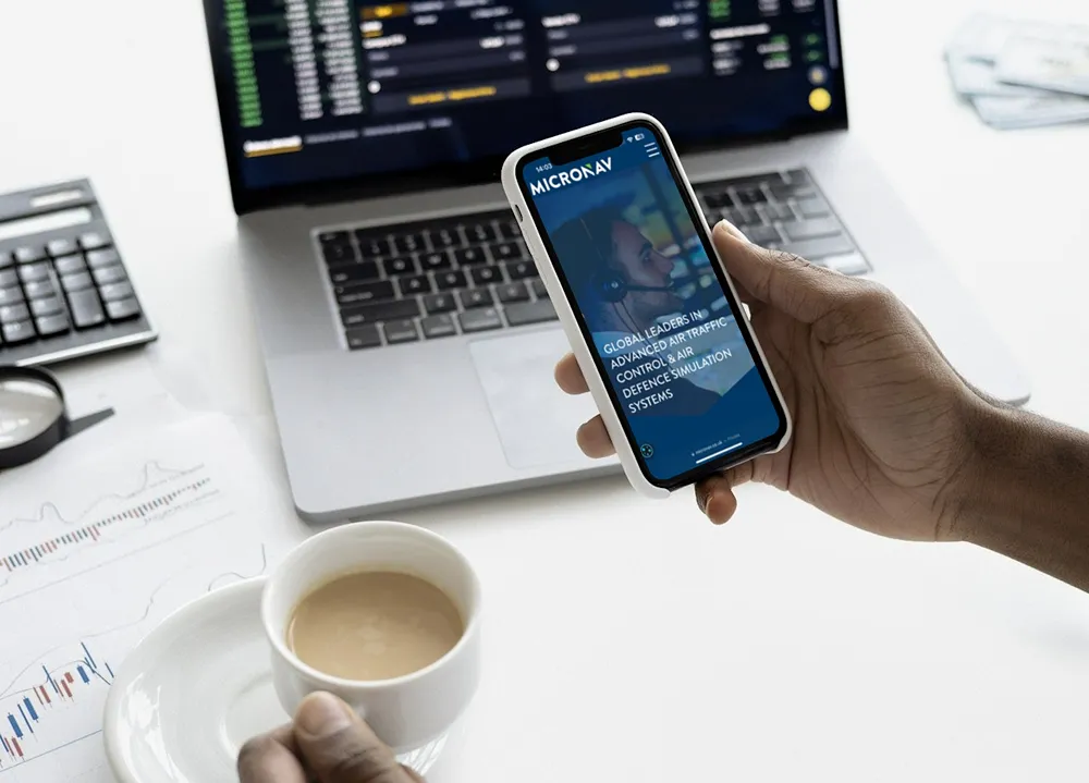 Micronav website homepage on a smartphone device in an office with a laptop in the background
