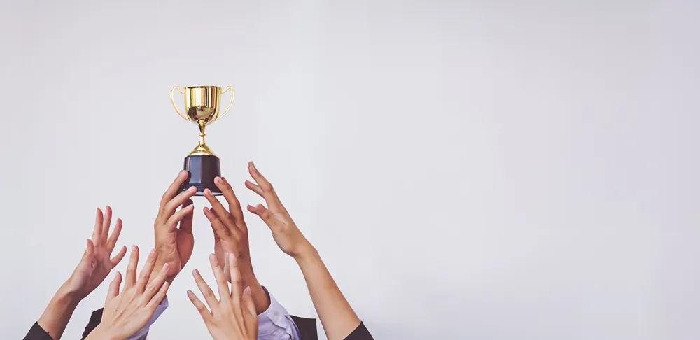3 people reaching upwards towards a golden trophy held aloft