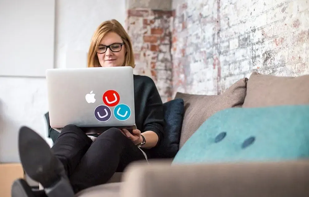 A person working on a laptop with three Umbraco stickers (red, dark blue, and teal) on it