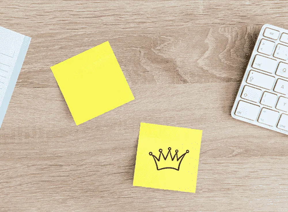 Two sticky notes on a tabletop, with a crown drawn on the lower of the two sticky notes.