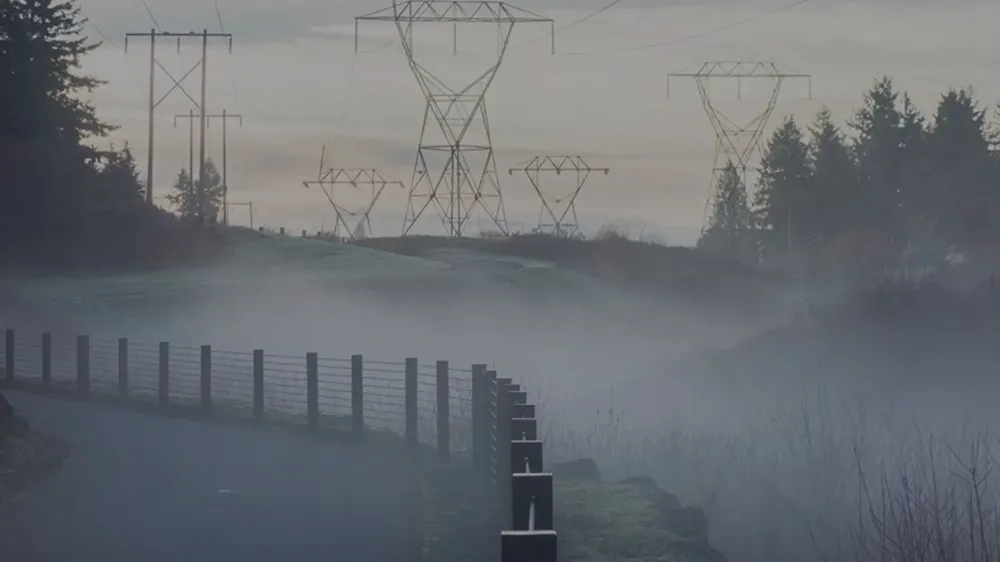 A road on a misty morning with electricity pylons in the background