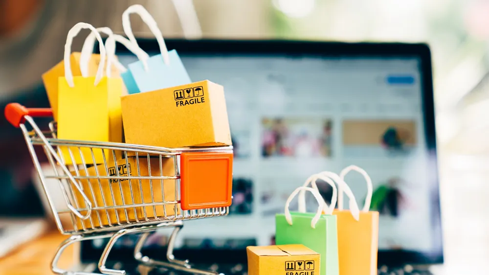 A small toy shopping cart full of mini boxes in front of a laptop.