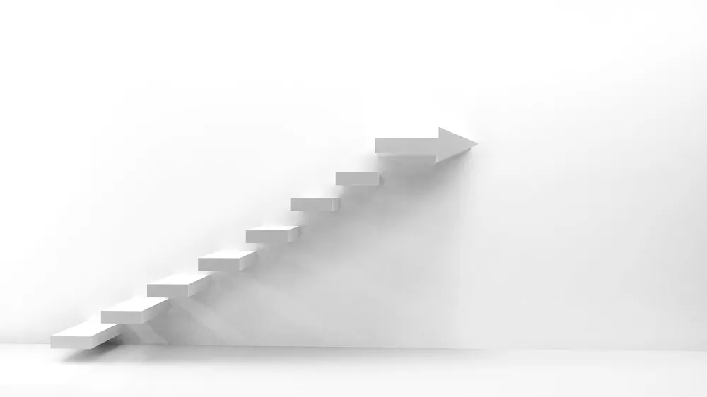 A set of white stairs in a white room, with the final step terminating in an arrow that points to the right.