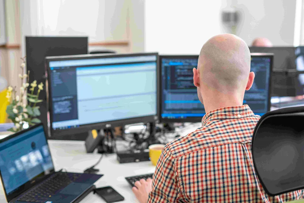 A person working at their desk with a laptop and two desktop monitors surrounding them