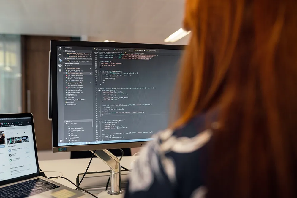 A person working at their desk, as they code on their desktop monitor